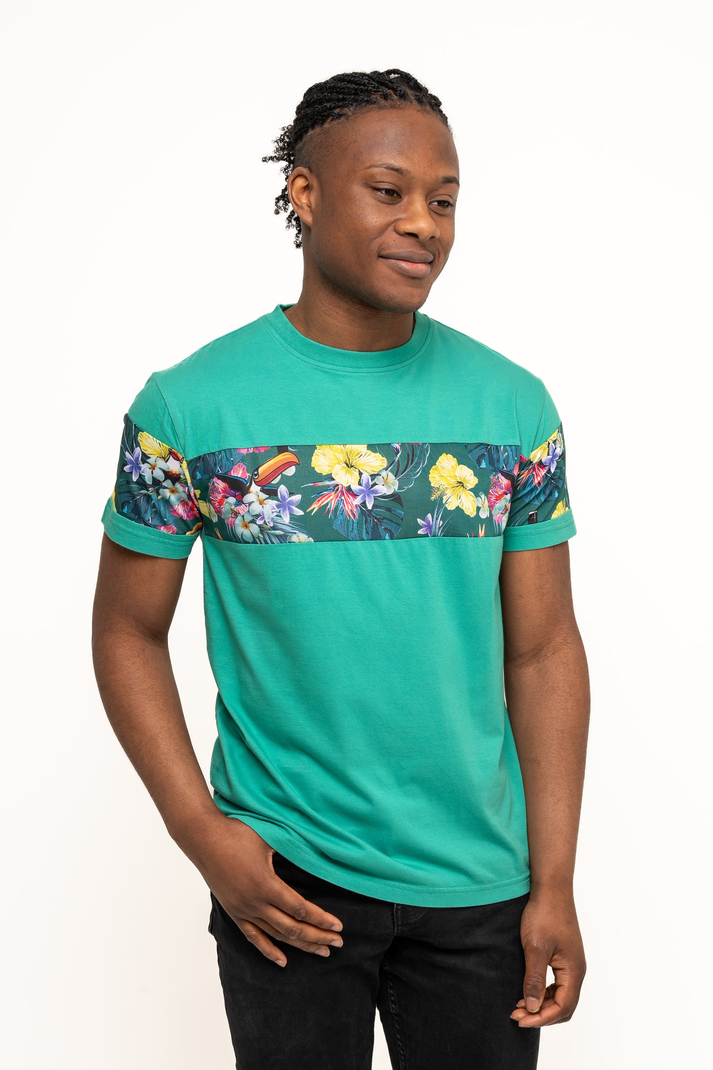A man stands against a white background, wearing the Guinness UK Toucan Hawaiian Green T-Shirt featuring a horizontal floral pattern and black pants—ideal for summer style.
