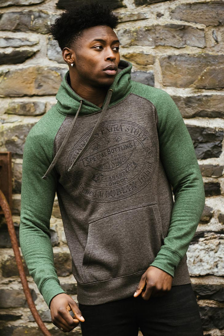 A man in a Guinness Grey and Green Hoodie from the Guinness Webstore UK stands before a stone wall, looking to his left.