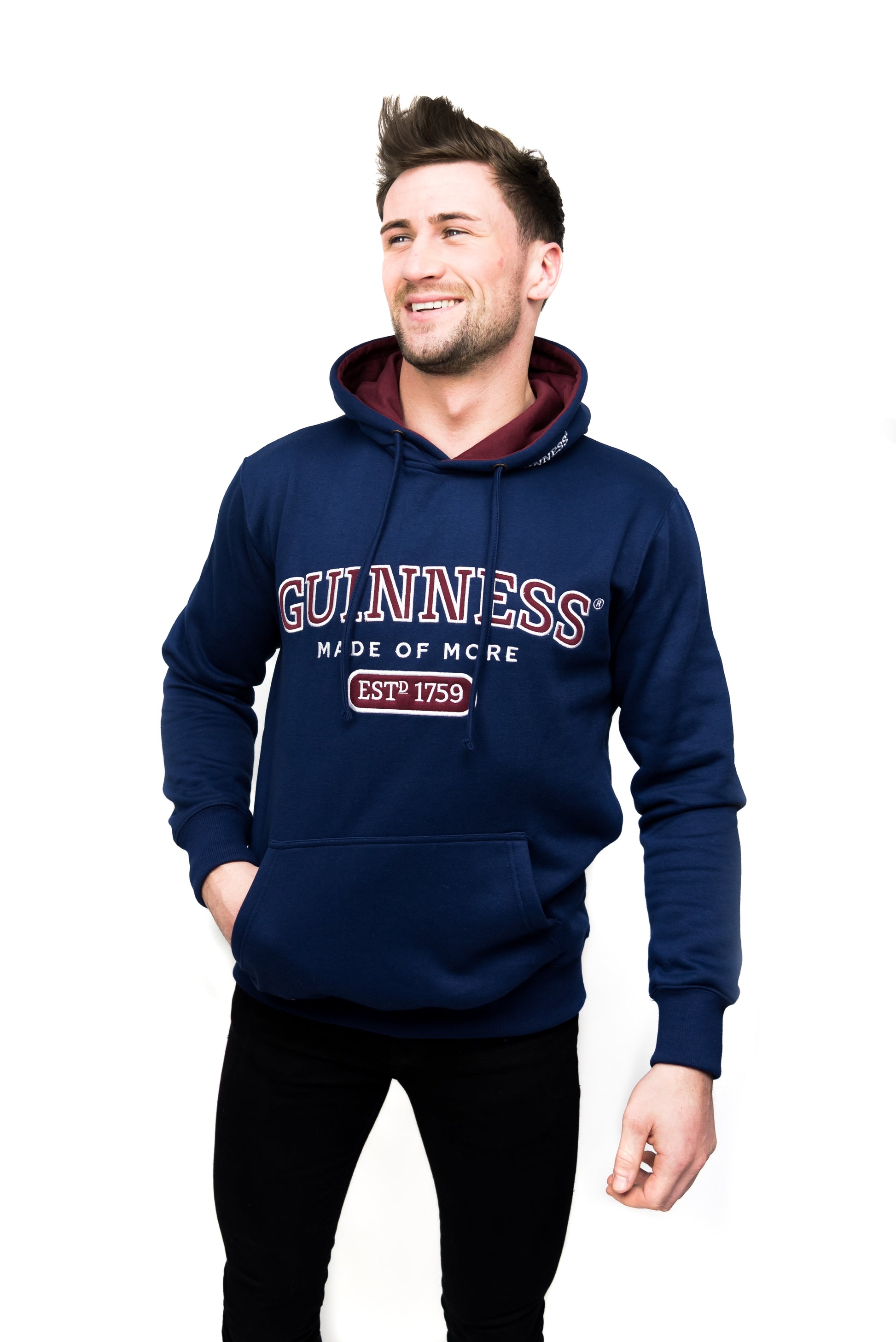 A young man wearing a navy hoodie with a red and white logo, resembling the Guinness UK Light Blue Hooded Sweatshirt.