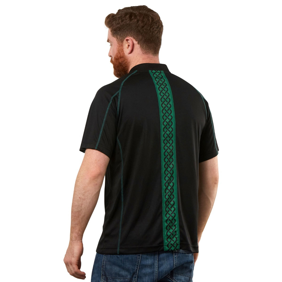 A man wears the Guinness Black & Green Short Sleeve Rugby Jersey by Guinness, showcasing a bold green Celtic pattern down the back, paired with blue jeans.