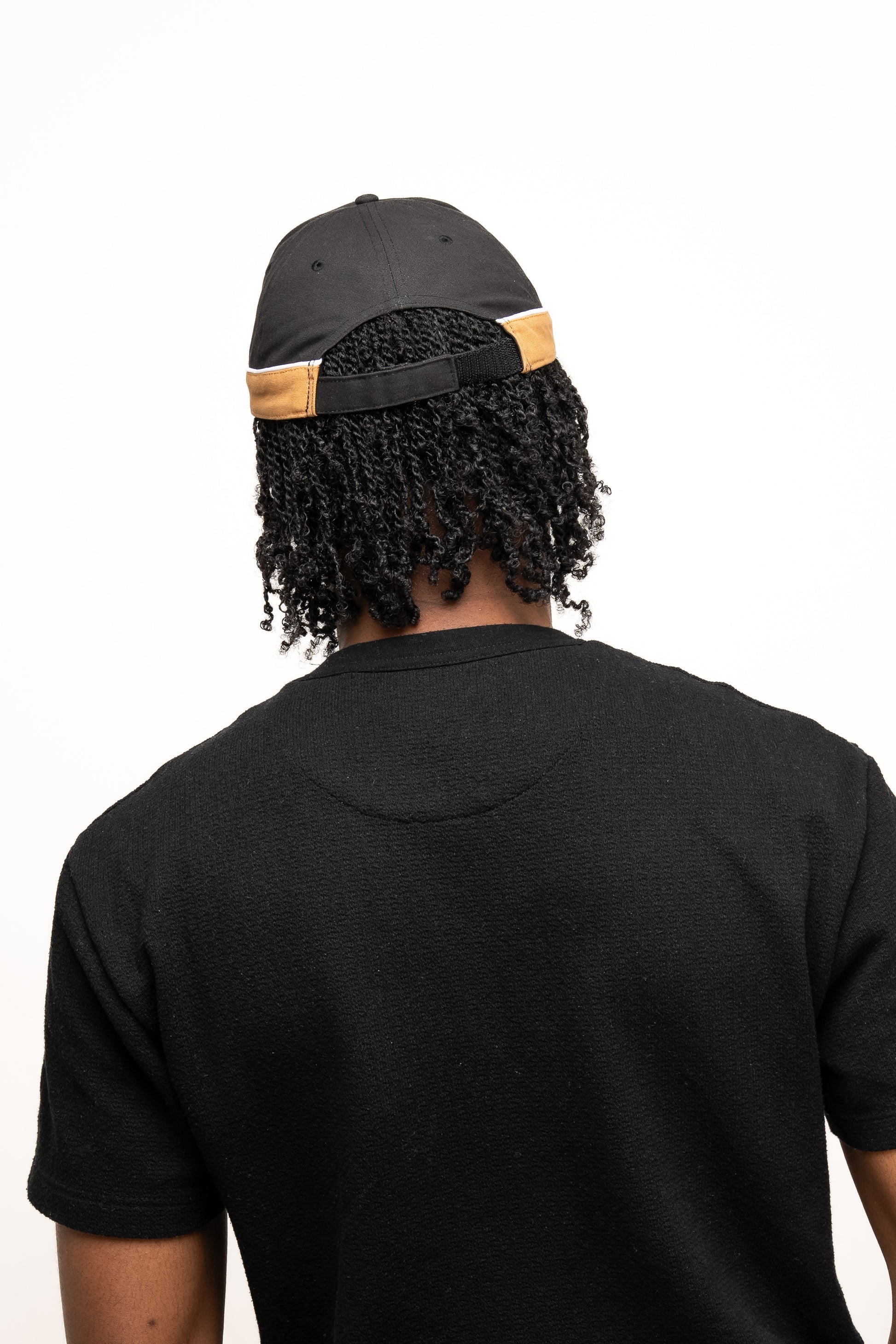 A person wearing a black t-shirt and the Guinness Webstore UK Black Cap with Caramel Edge is shown from the back against a plain white background.