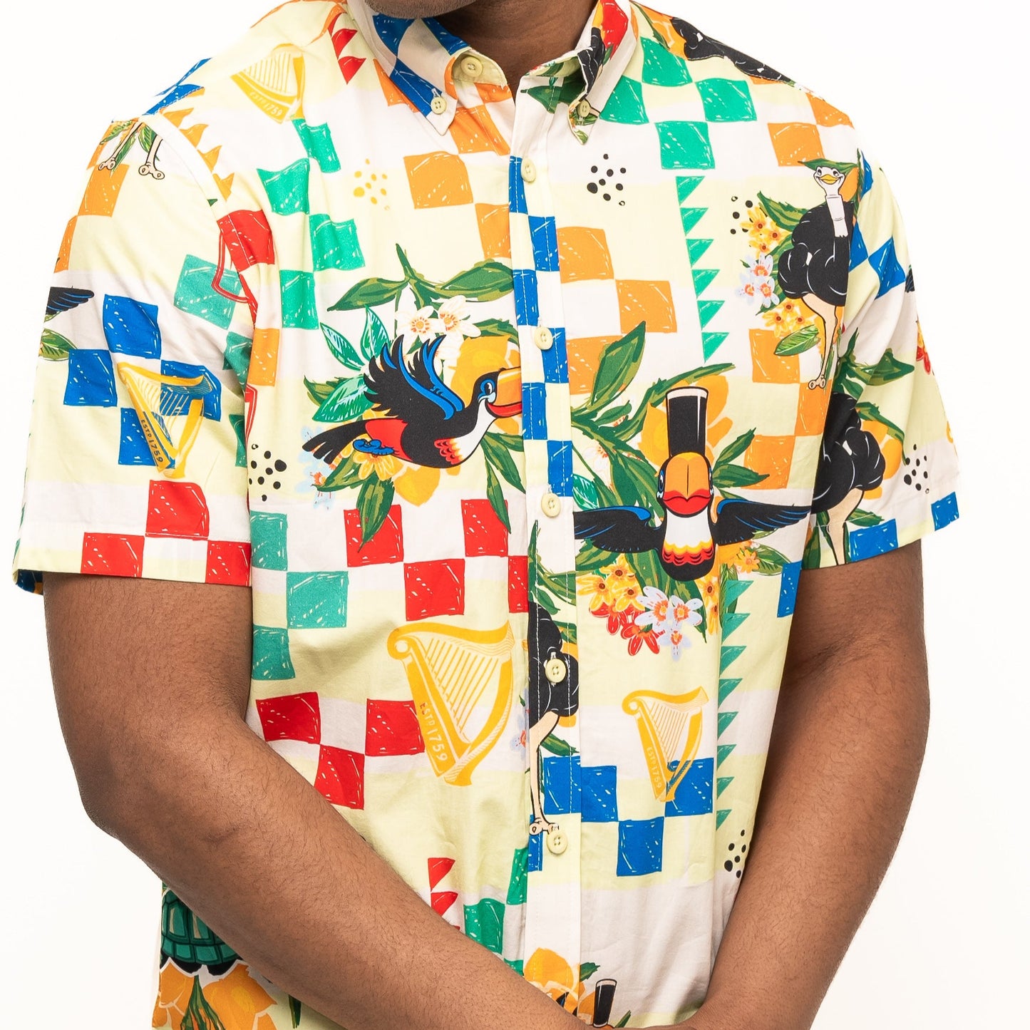 A person wears the brightly colored Guinness Toucan Beach Shirt by Guinness Webstore UK, a short-sleeve Hawaiian-style button-up with geometric and bird patterns, standing against a white background.