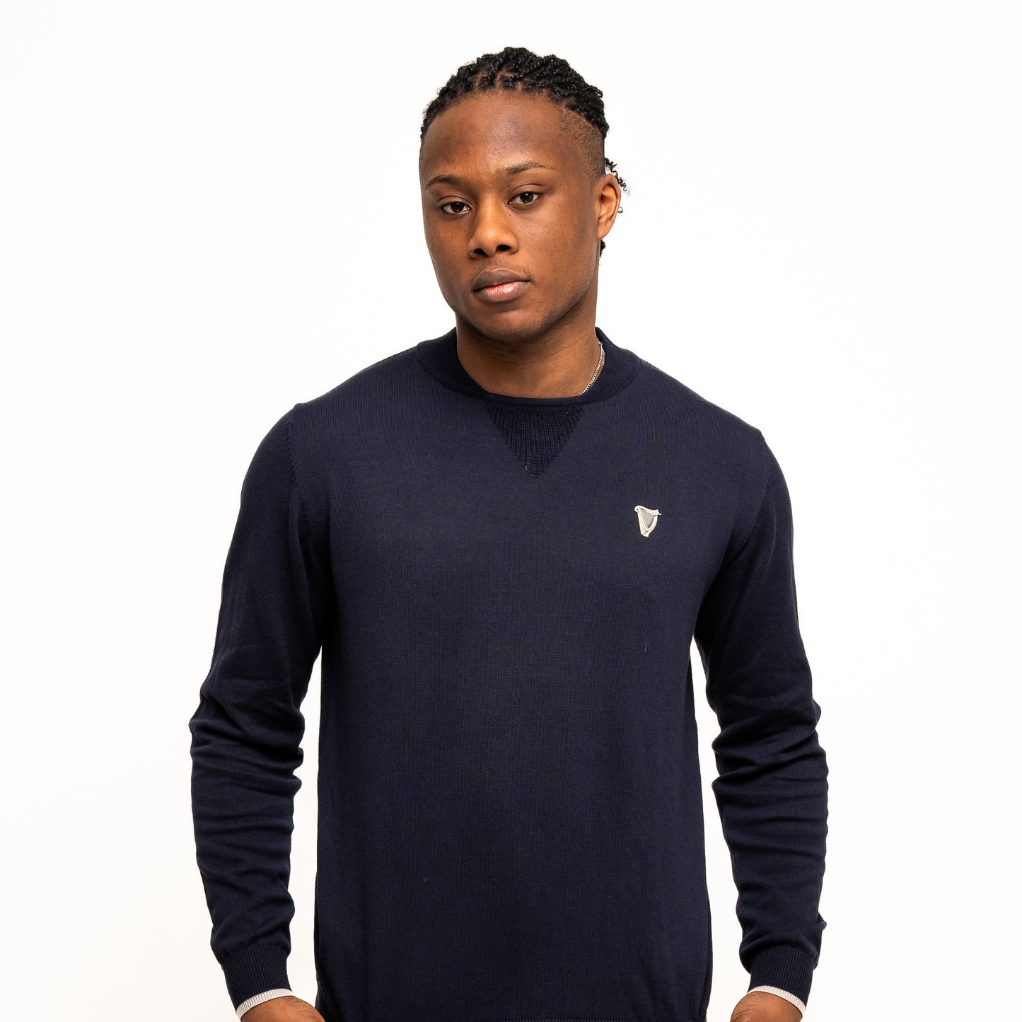 Against a white background, a person wears the Guinness Webstore UK's navy Guinness Performance Cotton Sweater, made with moisture-wicking cotton, paired with matching navy shorts and holds the sweater's hem.