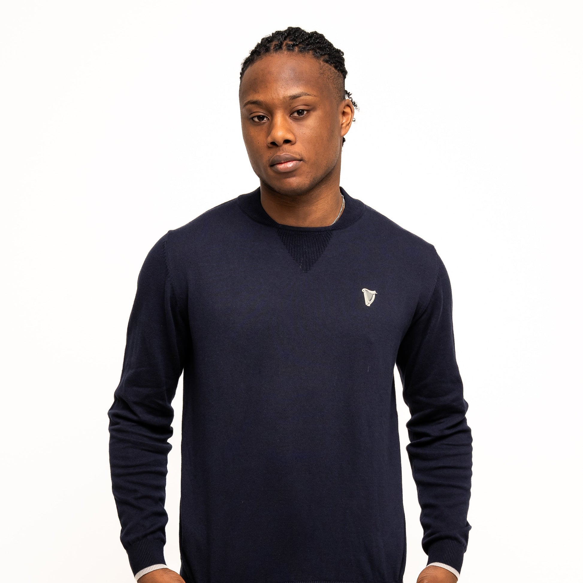 Against a white background, a person wears the Guinness Webstore UK's navy Guinness Performance Cotton Sweater, made with moisture-wicking cotton, paired with matching navy shorts and holds the sweater's hem.