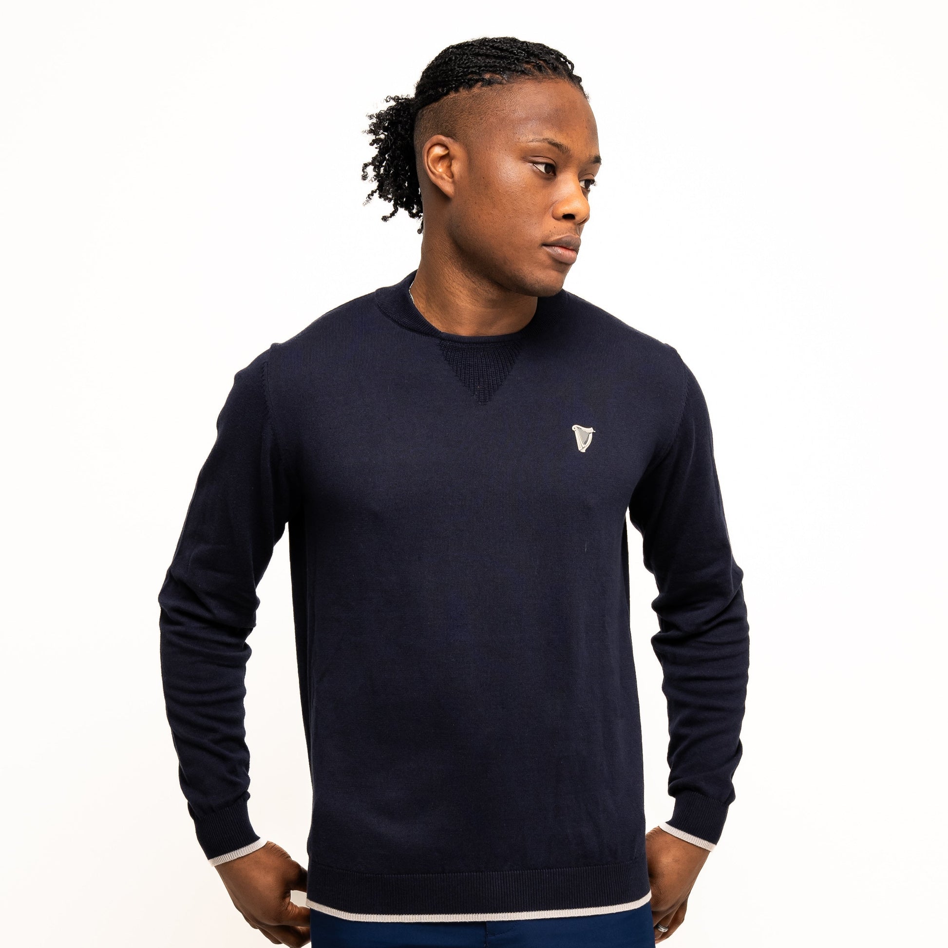 A person stands against a white background wearing the Guinness Webstore UK’s Guinness Performance Cotton Sweater - Navy with a small crest, paired with matching navy shorts, looking slightly to the side and hands near their pockets.