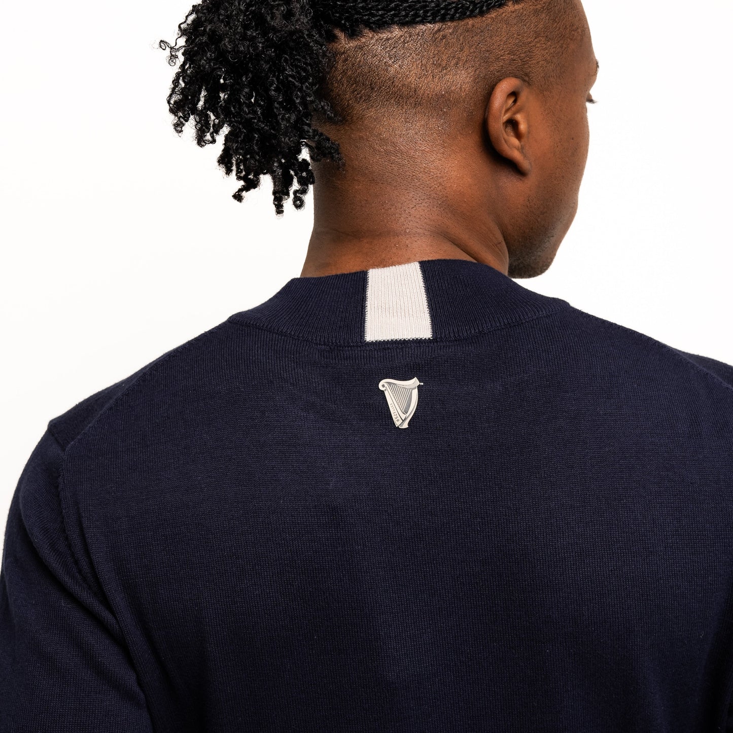 A person with braided hair in a ponytail is wearing the Guinness Performance Cotton Sweater - Navy from Guinness Webstore UK, featuring moisture-wicking cotton and a small white emblem on the upper back—perfect for golf days.