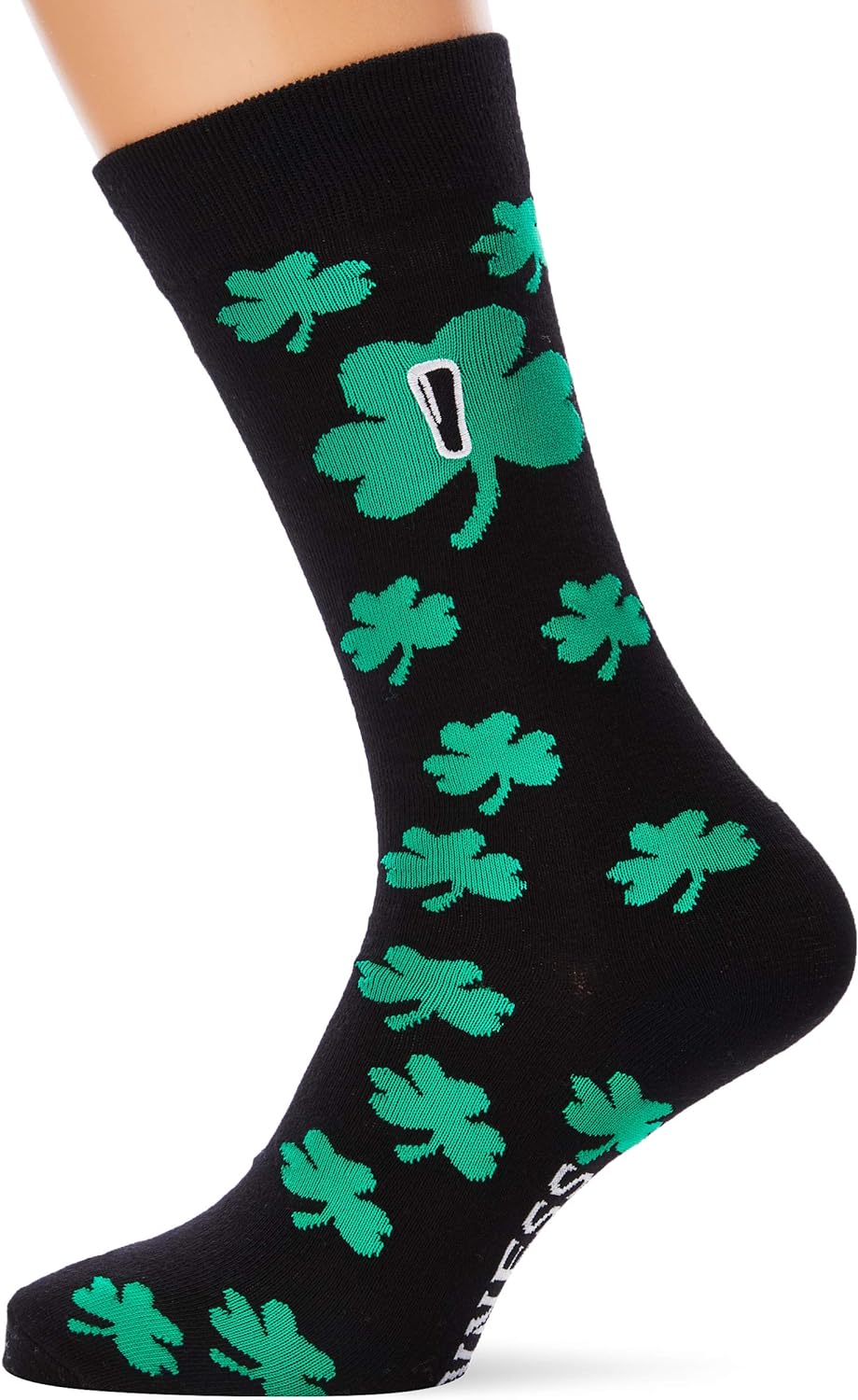 A person wearing a pair of black Guinness Shamrock Socks decorated with green shamrocks and a small, white rectangular Guinness logo near the calf.