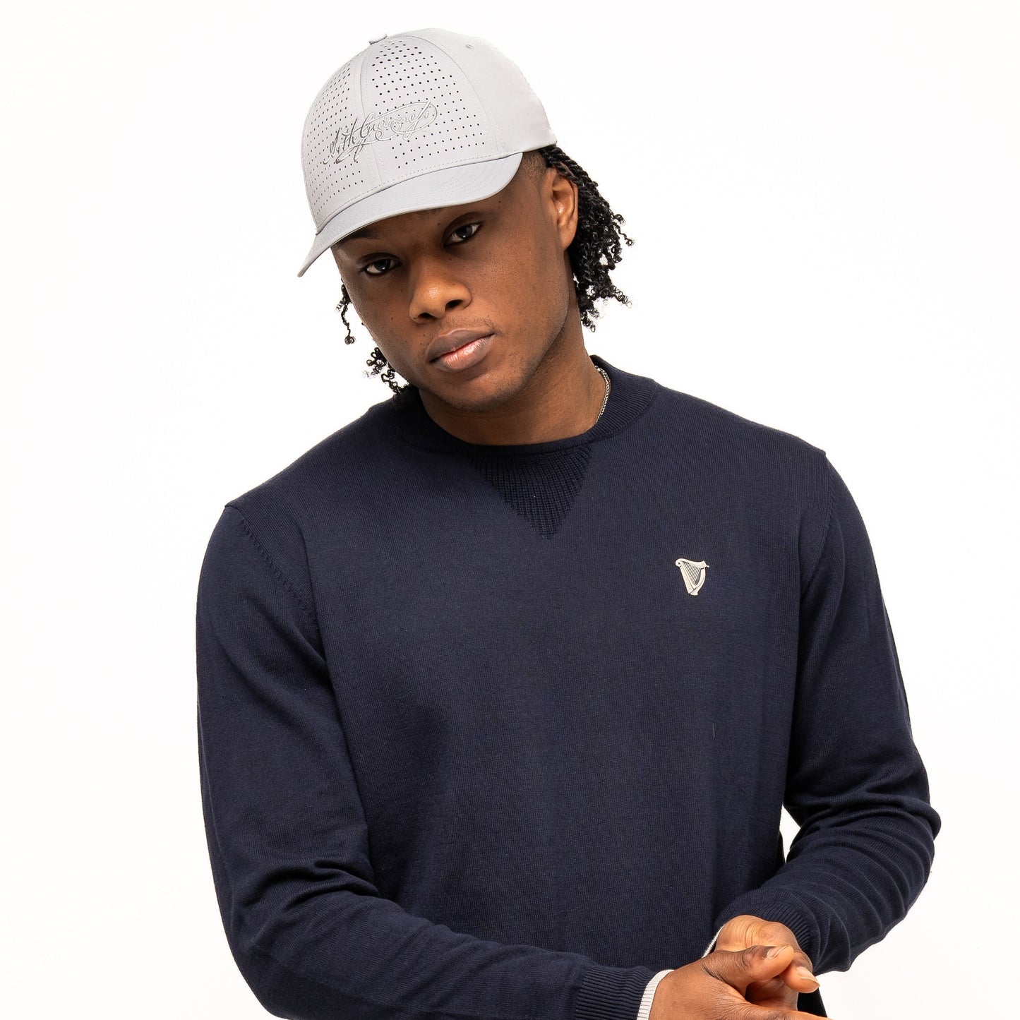 A person wearing a gray cap, blue pants, and the Guinness Performance Cotton Sweater - Navy by Guinness Webstore UK stands against a plain white background.