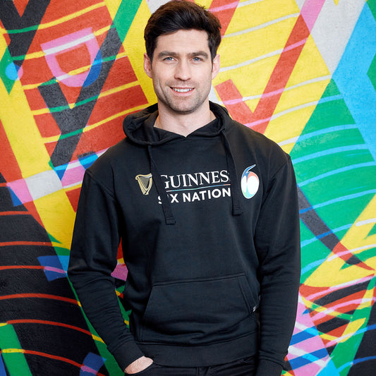 Man in a black Guinness Six Nations Rugby Hoodie standing in front of a colorful graffiti wall.