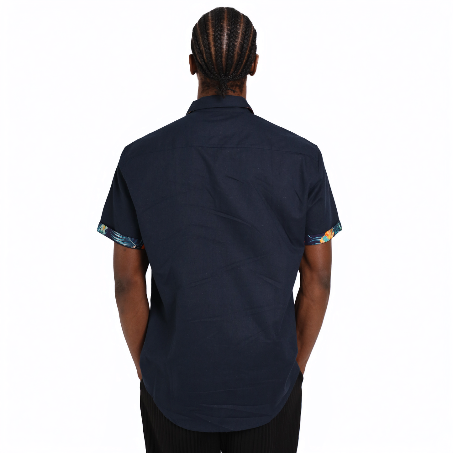 A person with braided hair is shown from the back wearing a short-sleeve Guinness Navy Linen Summer Shirt from Guinness Webstore UK, featuring patterned sleeve cuffs.