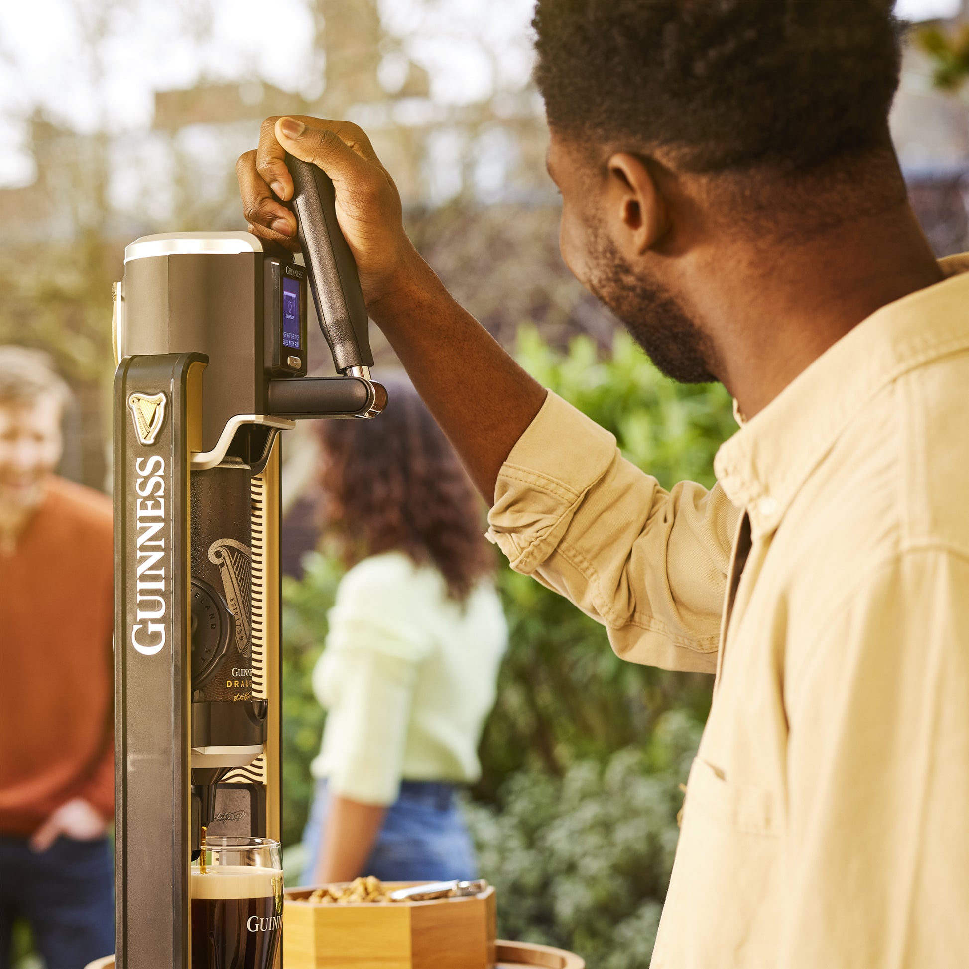 At an outdoor gathering, a person operates a Guinness MicroDraught from Guinness UK while others stand in the background, creating a perfect home bar vibe.
