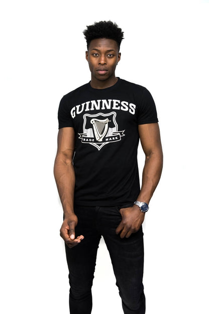 A man wearing a black graphic Guinness Black Trademark Label T-Shirt featuring the iconic Guinness UK logo.