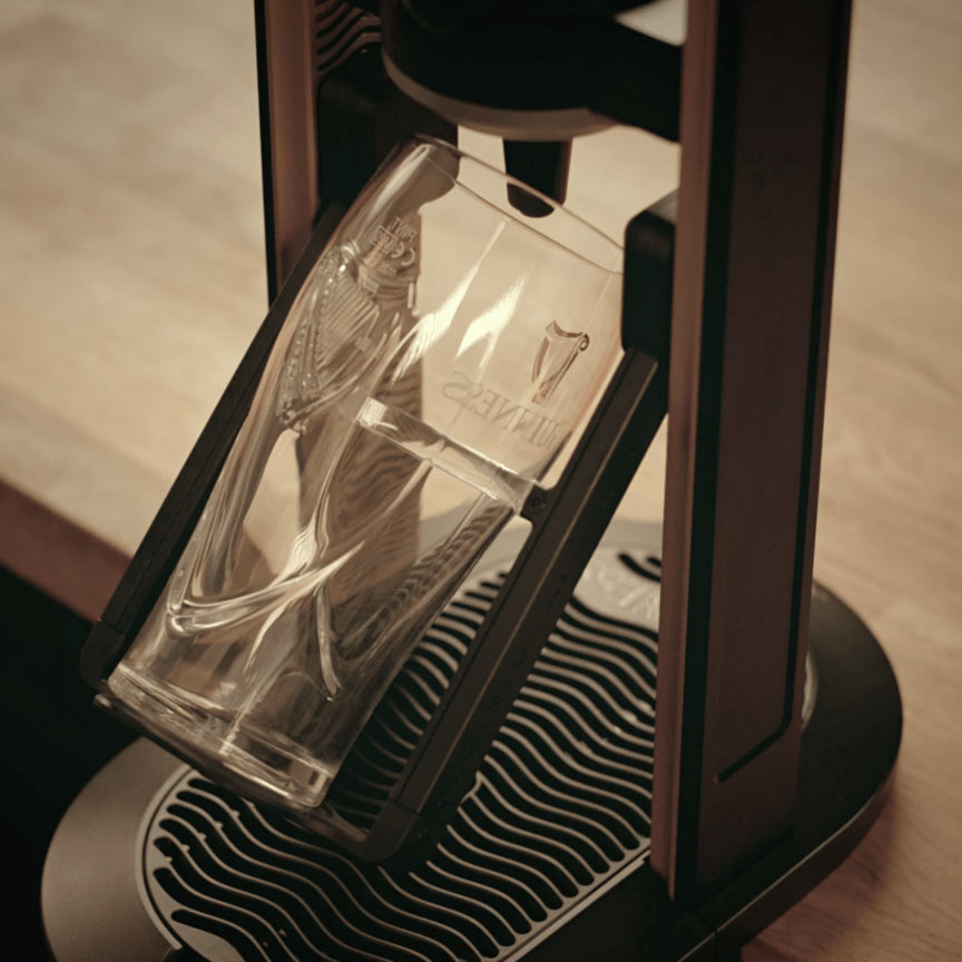 A Draught Guinness glass is sitting on top of a Guinness UK MicroDraught machine, perfect for a home bar setup.