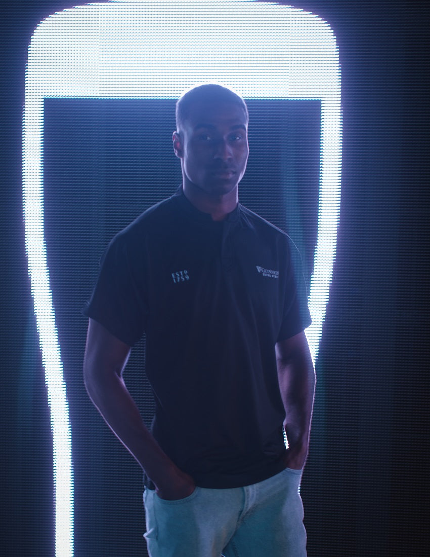A man in a black shirt with Guinness's All Black Rugby Jersey fabric standing in front of a neon light.
