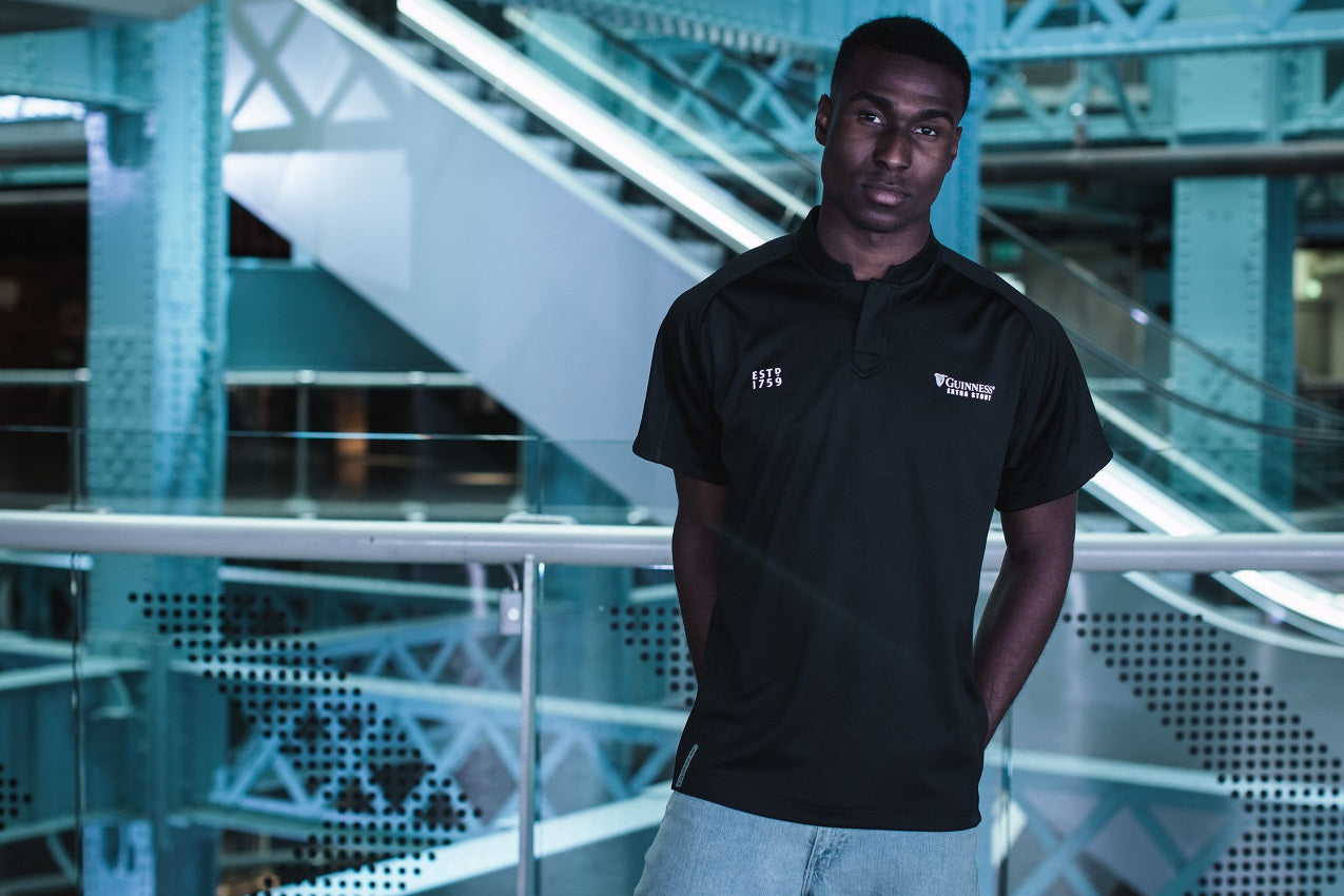 A man in a black polo shirt, wearing a Guinness All Black Rugby Jersey, standing on an escalator.