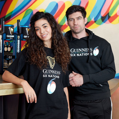 Two people posing in front of a bar wearing black Guinness UK Six Nations Black T-shirts.