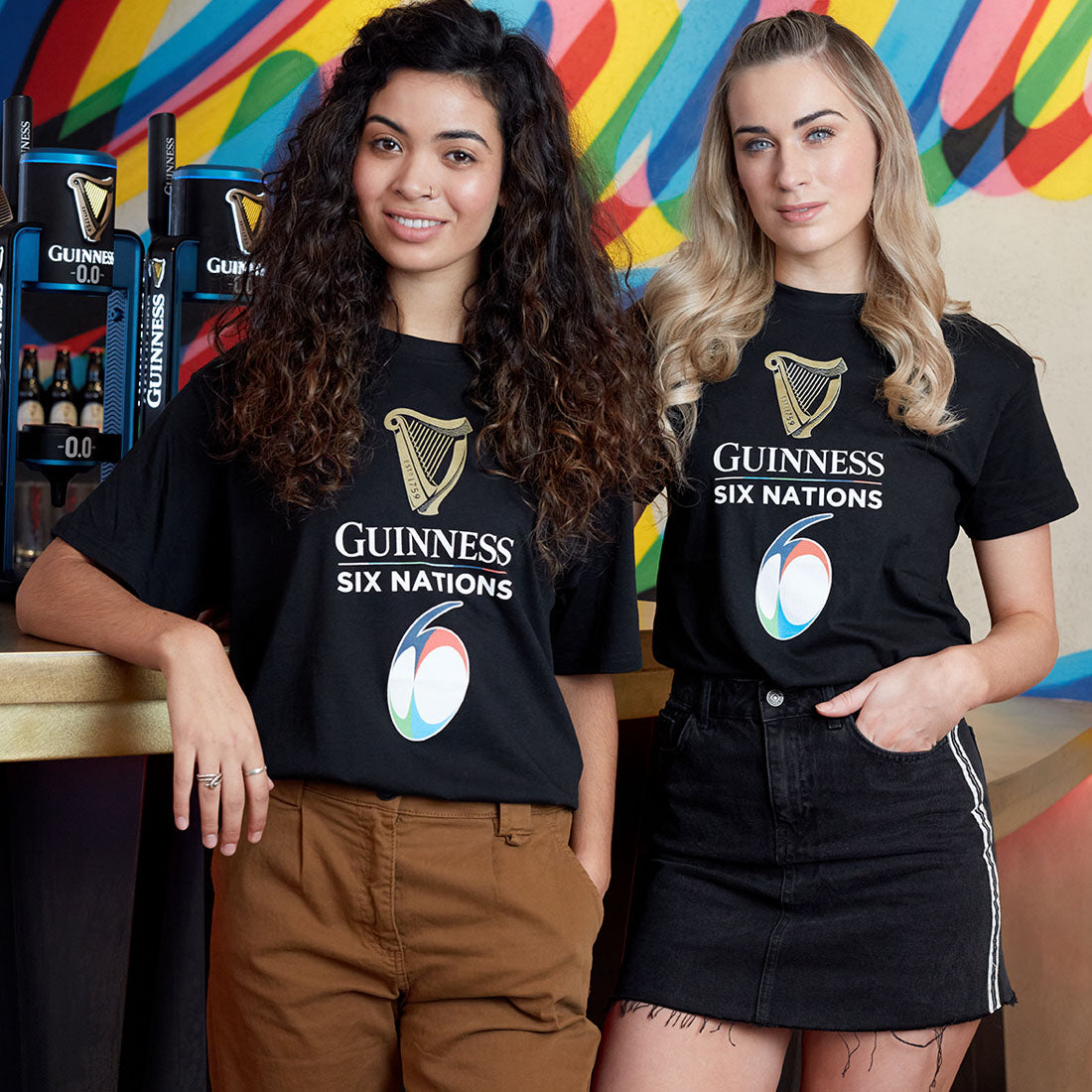 Two women standing in front of a bar wearing black Guinness UK Six Nations t-shirts.