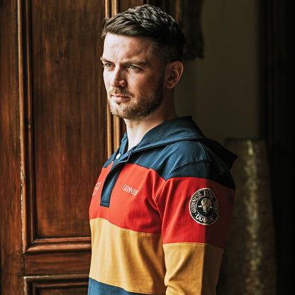 A man in a colorful striped Guinness hooded rugby jersey standing in front of a door.