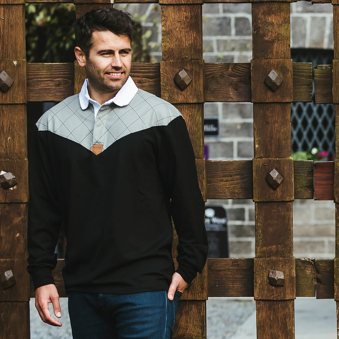 A man in a Guinness Heritage Charcoal Grey and Black Long Sleeve Rugby Jersey from Guinness UK is standing next to a wooden fence.