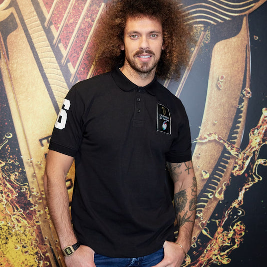 A man in a Guinness UK black polo shirt standing in front of a wall, representing the spirit of Six Nations.
