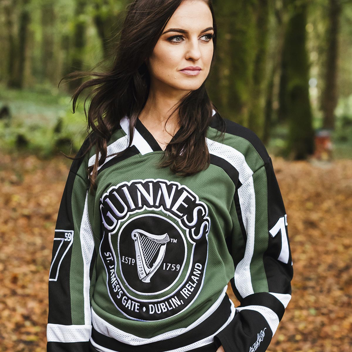 A woman wearing a Guinness UK HARP hockey jersey in the woods.