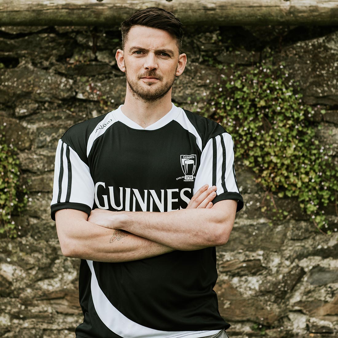 A man in a black and white Guinness® Soccer Jersey standing in front of a stone wall.