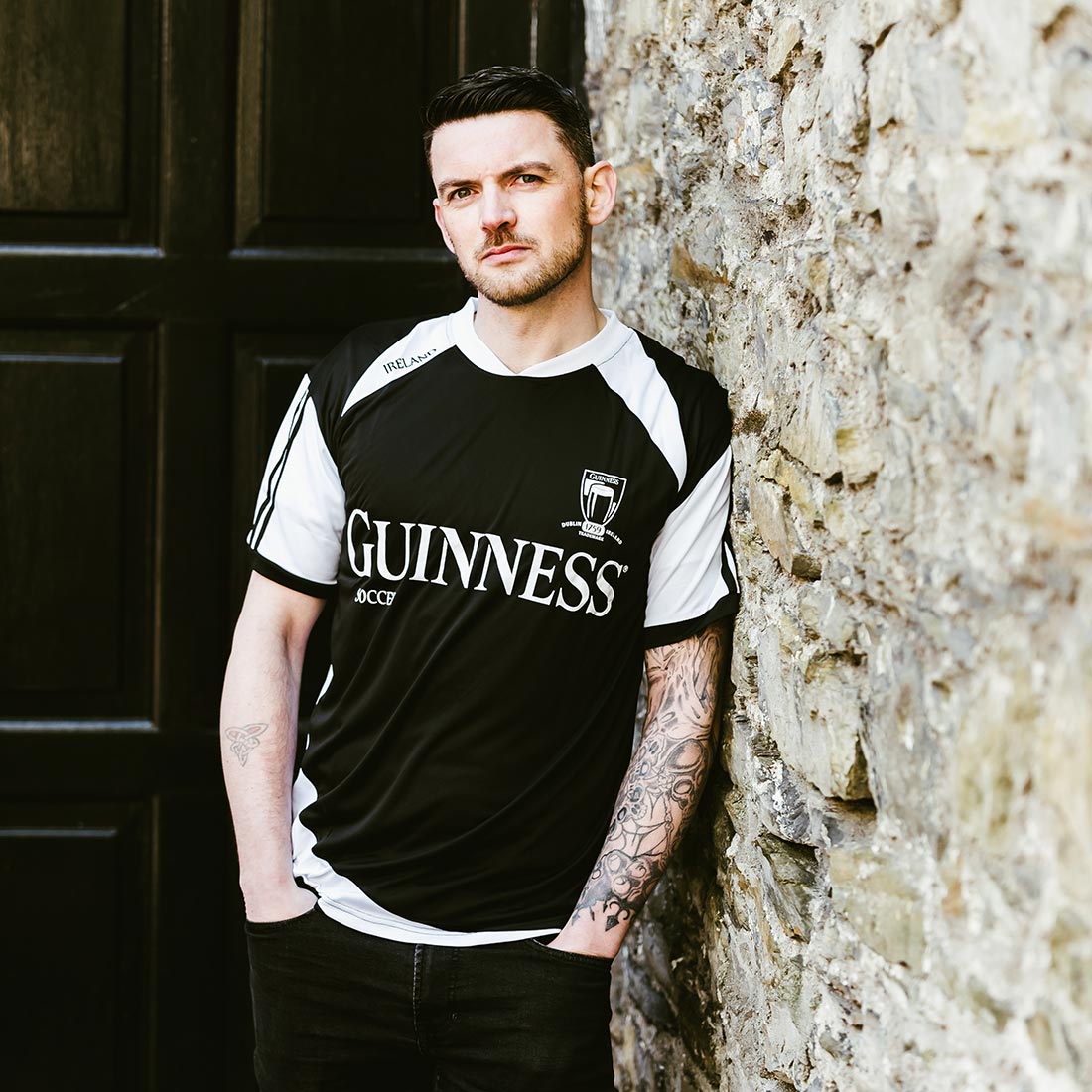 A man in a black and white Guinness® Soccer Jersey leaning against a wall.