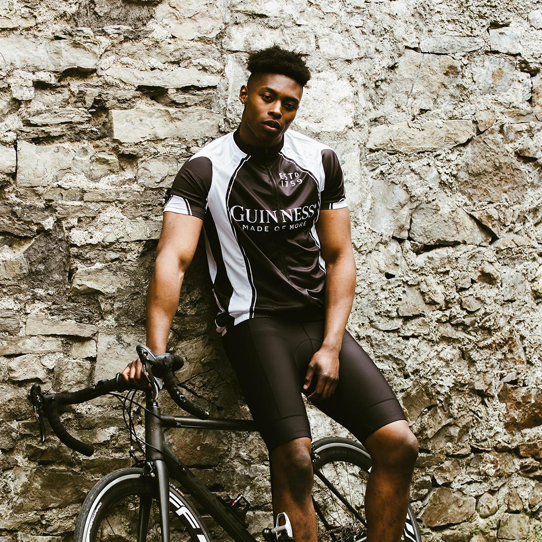 A man leaning against a stone wall with a Guinness Performance Cycling Jersey from Guinness UK.