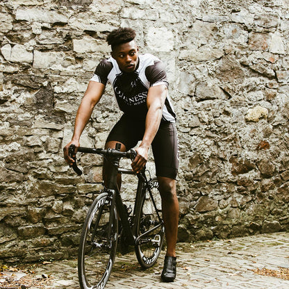 A man wearing a Guinness UK Cycling Jersey is riding a bike in front of a stone wall.