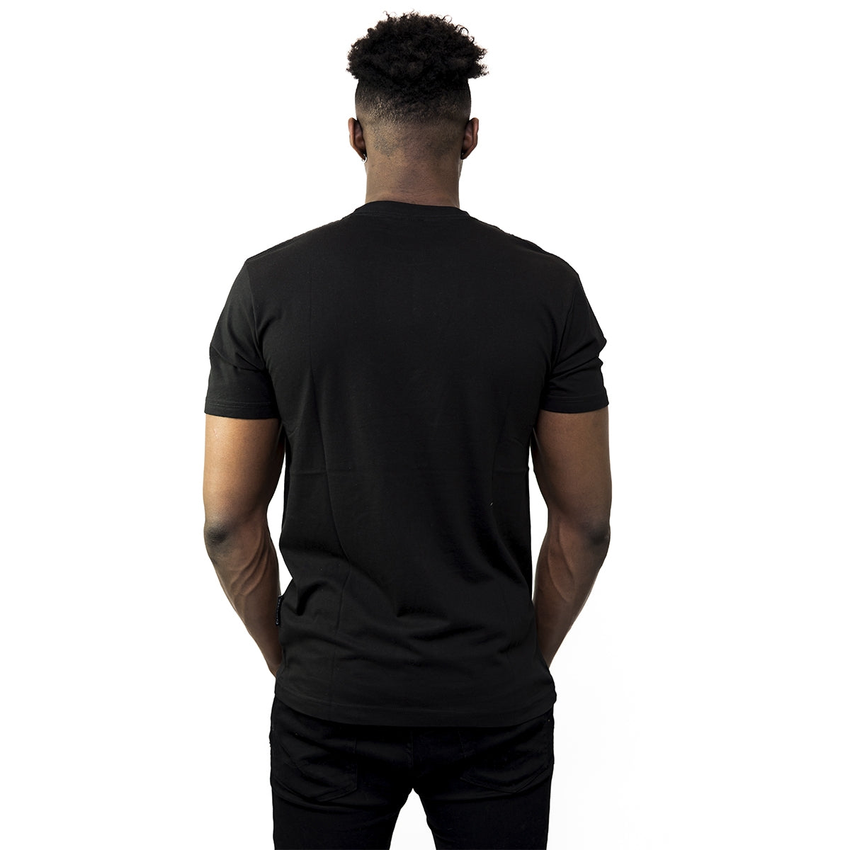 A man faces away from the camera, wearing a Guinness® Distressed Gaelic Label T-Shirt by Guinness UK and black pants, set against a white background.