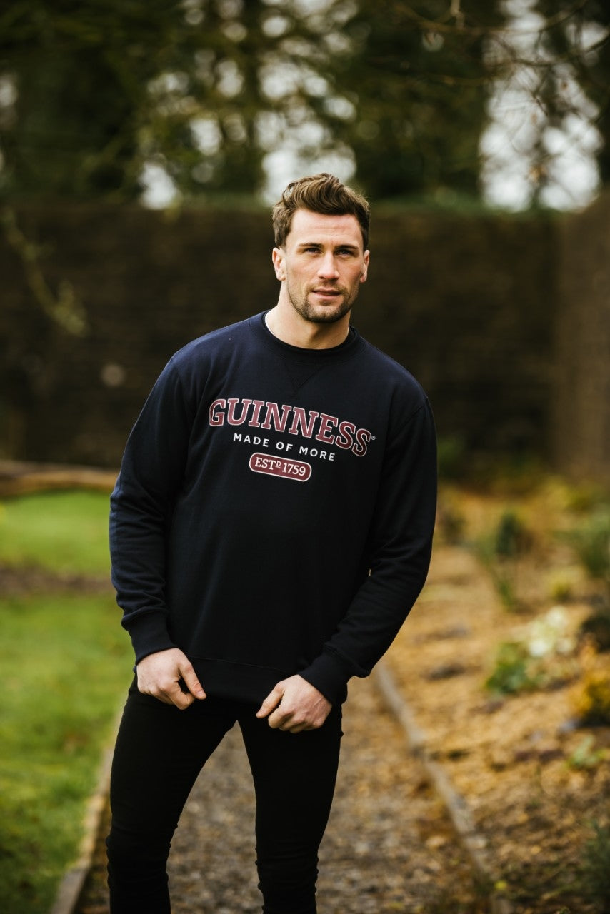 A man wearing a Guinness UK Navy Crew Neck Sweater standing in a garden, exuding a smart casual look perfect for chilly cold winters.