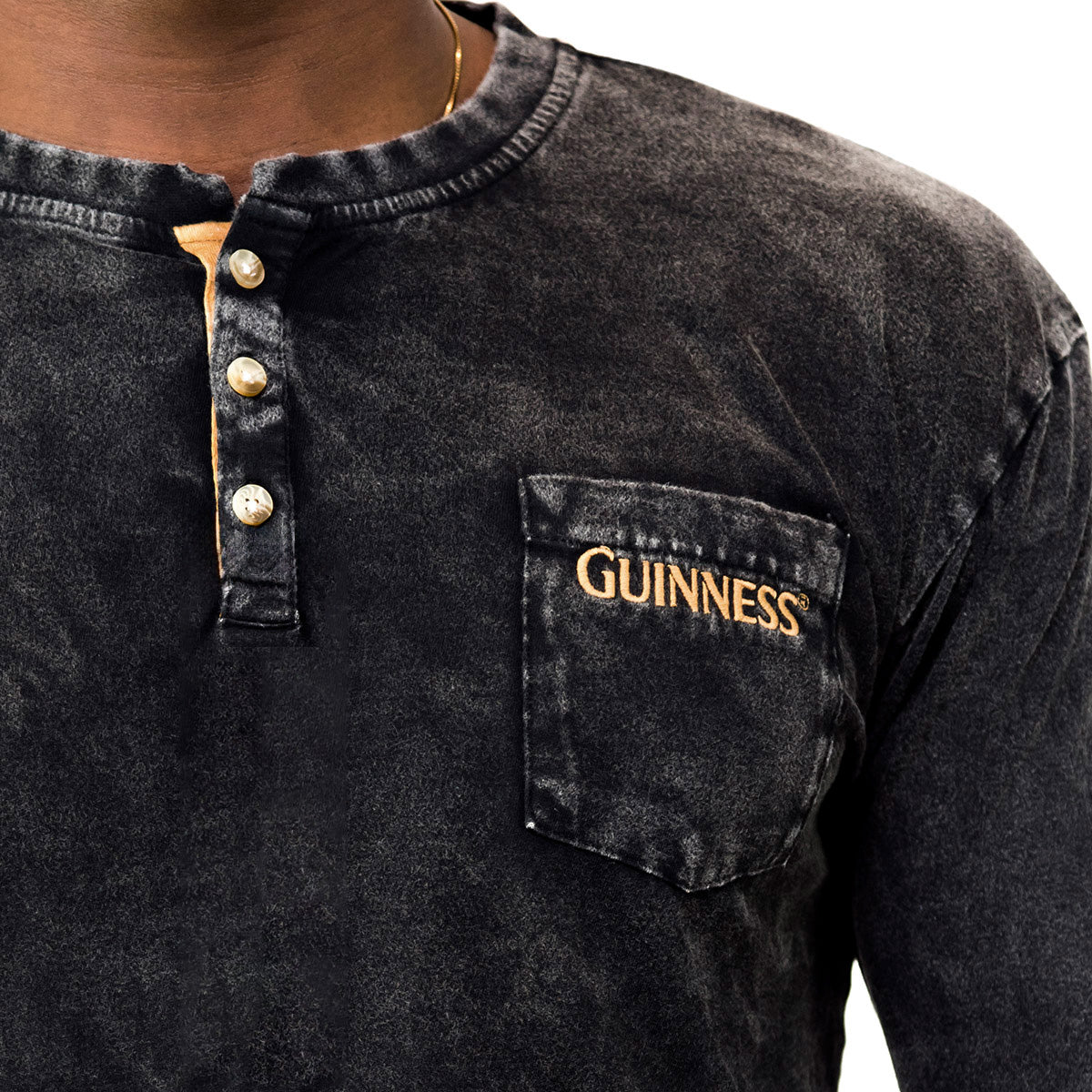 A person wearing a black, faded Guinness Classic Henley featuring three buttons and a chest pocket embroidered with "Guinness" in yellow.