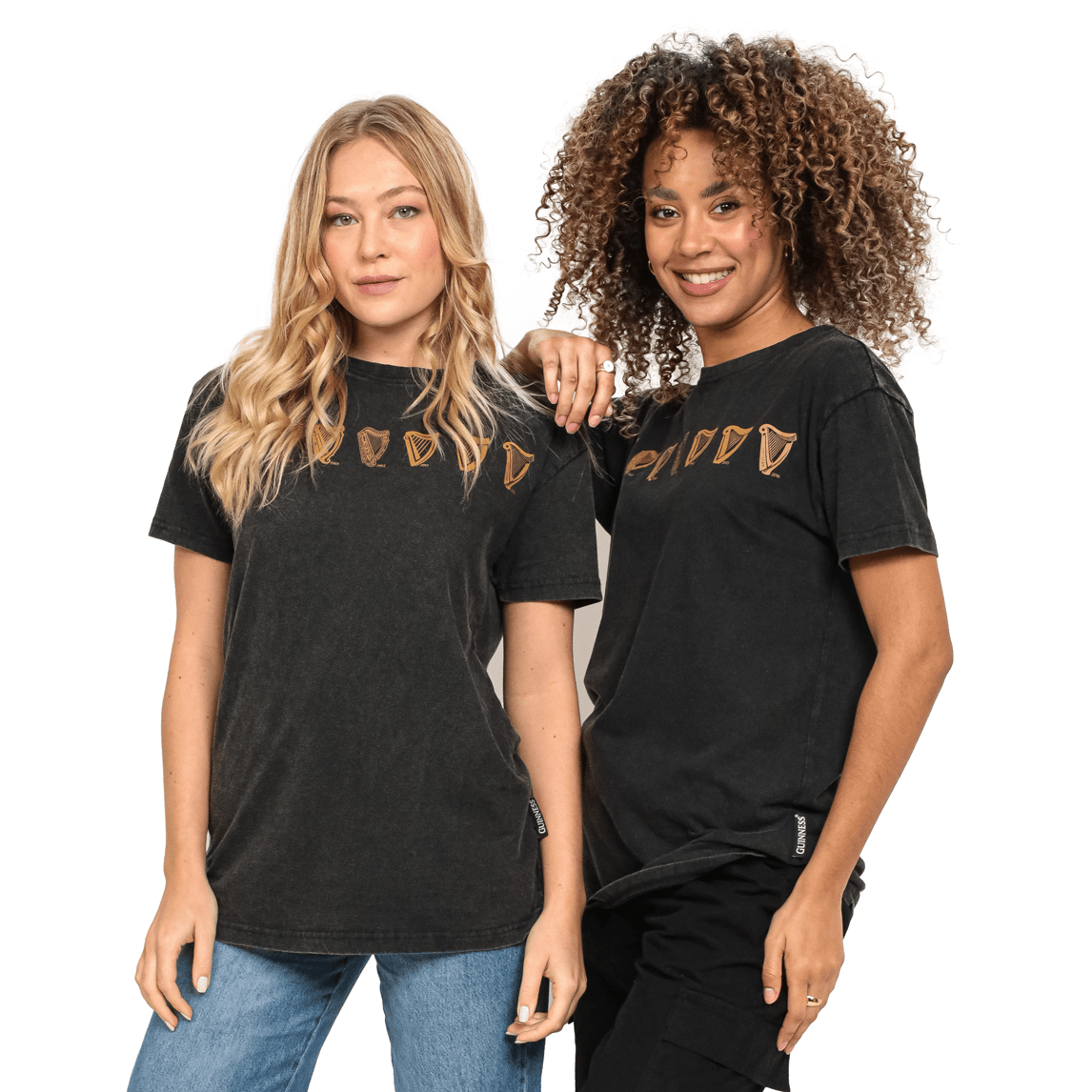 Two women wearing cotton black t-shirts, one of which is the Guinness UK Evolution Harp Tee.