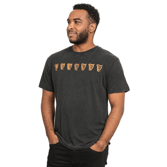 A man wearing a black Evolution Harp Tee, made of cotton, with golden shields on it from Guinness UK.