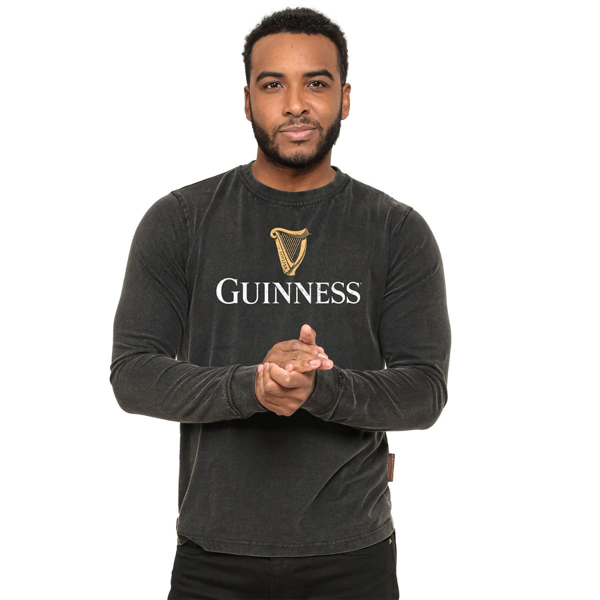 A man in a black Guinness® Premium Harp Jumper standing with his hands clasped in front of him on a white background.