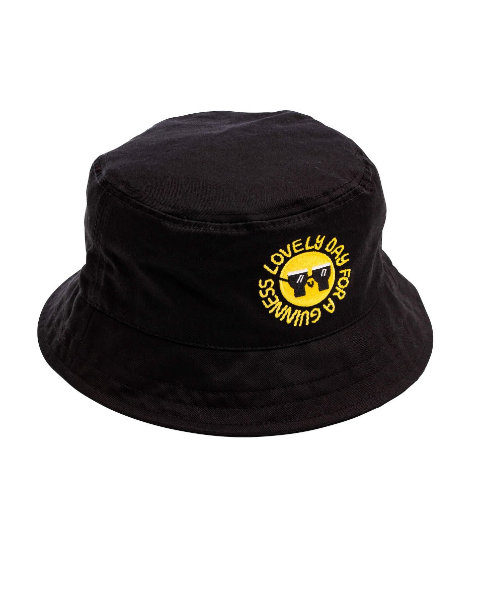 A stylish black FATTI BURKE "LOVELY DAY FOR A GUINNESS" bucket hat with a vibrant yellow Guinness Webstore UK logo, perfect for festival season and summer.