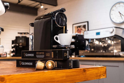 A Guinness UK-branded Guinness 232 Coffee Capsules machine sits on a table in a coffee shop.