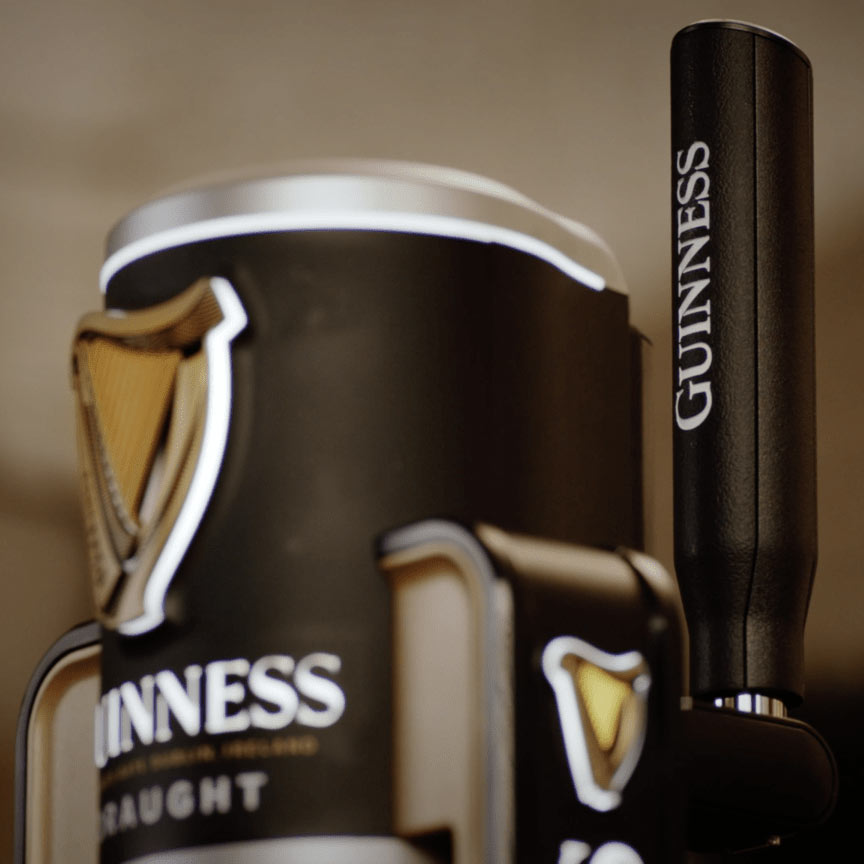 Close-up of a Guinness® beer tap in a home bar, featuring the recognizable harp logo on the handle and a pint glass, showcasing Guinness MicroDraught by Guinness UK prominently.