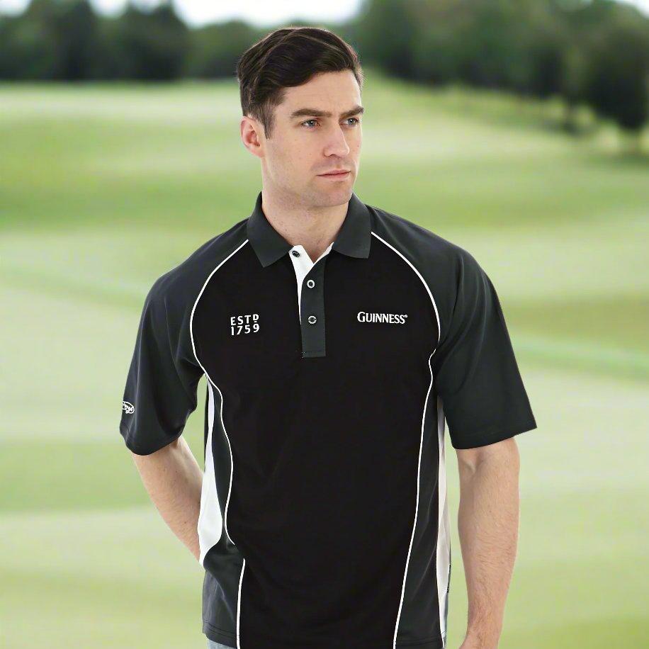 A man stands wearing a black Guinness Golf Shirt with "ESTD 1759" and "GUINNESS" logos, paired with distressed blue jeans.