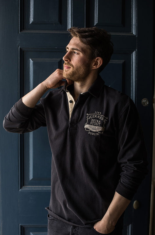 A man wearing a Classic Rugby Jersey with Guinness branding leaning against a door.