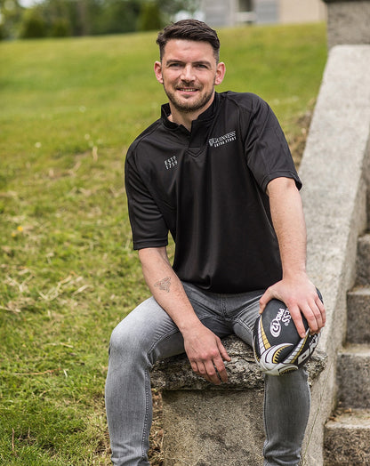 A man sitting on steps holding a football, showcasing the Guinness UK All Black Rugby Jersey.