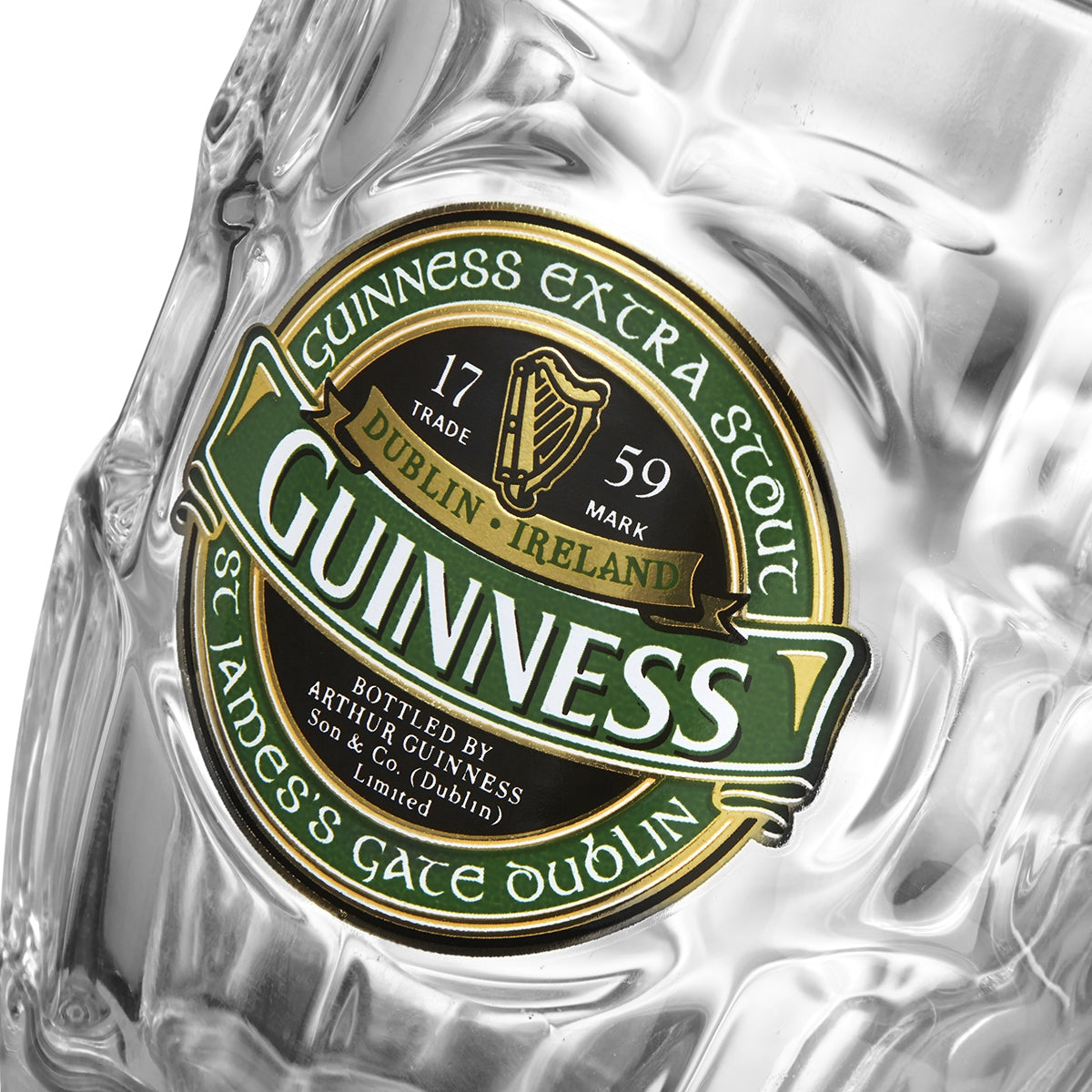 Close-up of a high-quality glass with a green and gold Guinness label indicating "Guinness Extra Stout" brewed in Dublin, Ireland in 1759. Text includes "St James's Gate Dublin" and "Arthur Guinness Son & Co. Ltd." Part of the exclusive Guinness Ireland Dimpled Tankard collection.