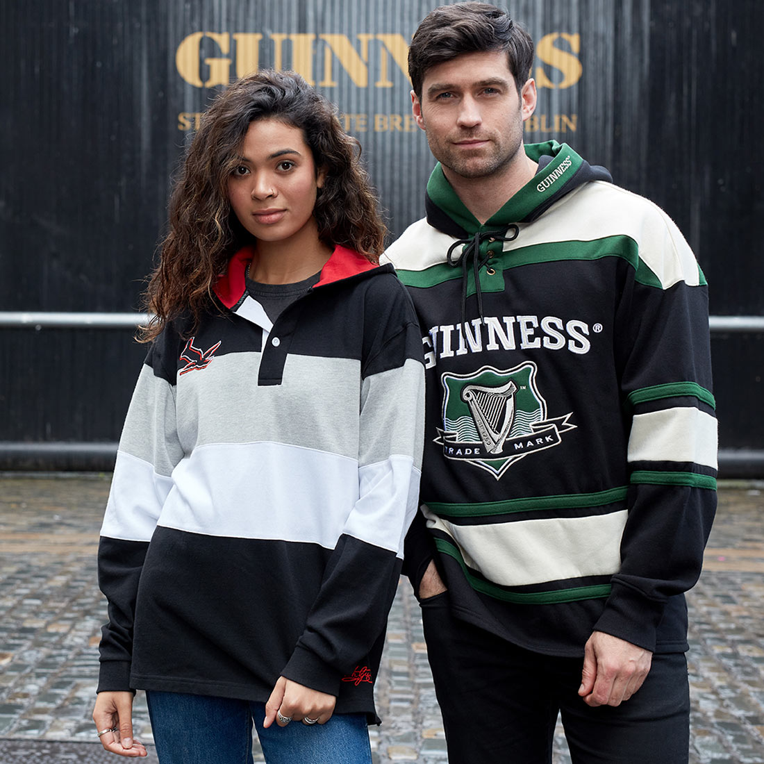 A rugby fan and a hooded woman standing in front of a Guinness UK Black & Red Toucan Hooded Rugby sign.