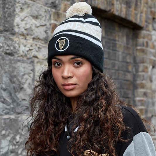 A young woman wearing a warm Guinness Black and White Premium Beanie with the Ireland flag on it, made by Guinness UK.