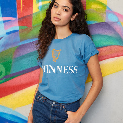 A woman donning a blue Sky Blue Guinness Harp Premium T-Shirt made of soft cotton material. (brand name: Guinness UK)
