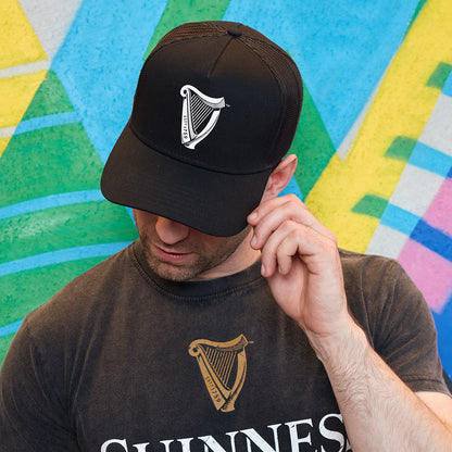 A man wearing a Guinness UK Premium Black & White Harp Cap in front of a colorful wall.