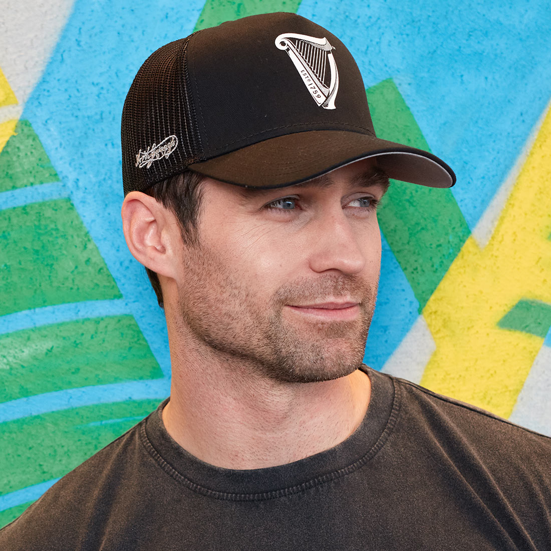 A man wearing a Guinness Premium Black & White Harp Cap in front of a colorful wall.