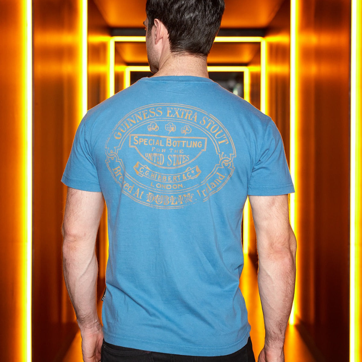 A man wearing a Sky Blue Guinness Harp Premium T-Shirt, made by Guinness UK, standing in a hallway.