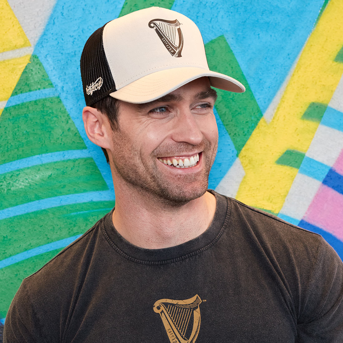 A man wearing a Guinness UK t-shirt and a Guinness Premium Beige with Black Harp Cap.