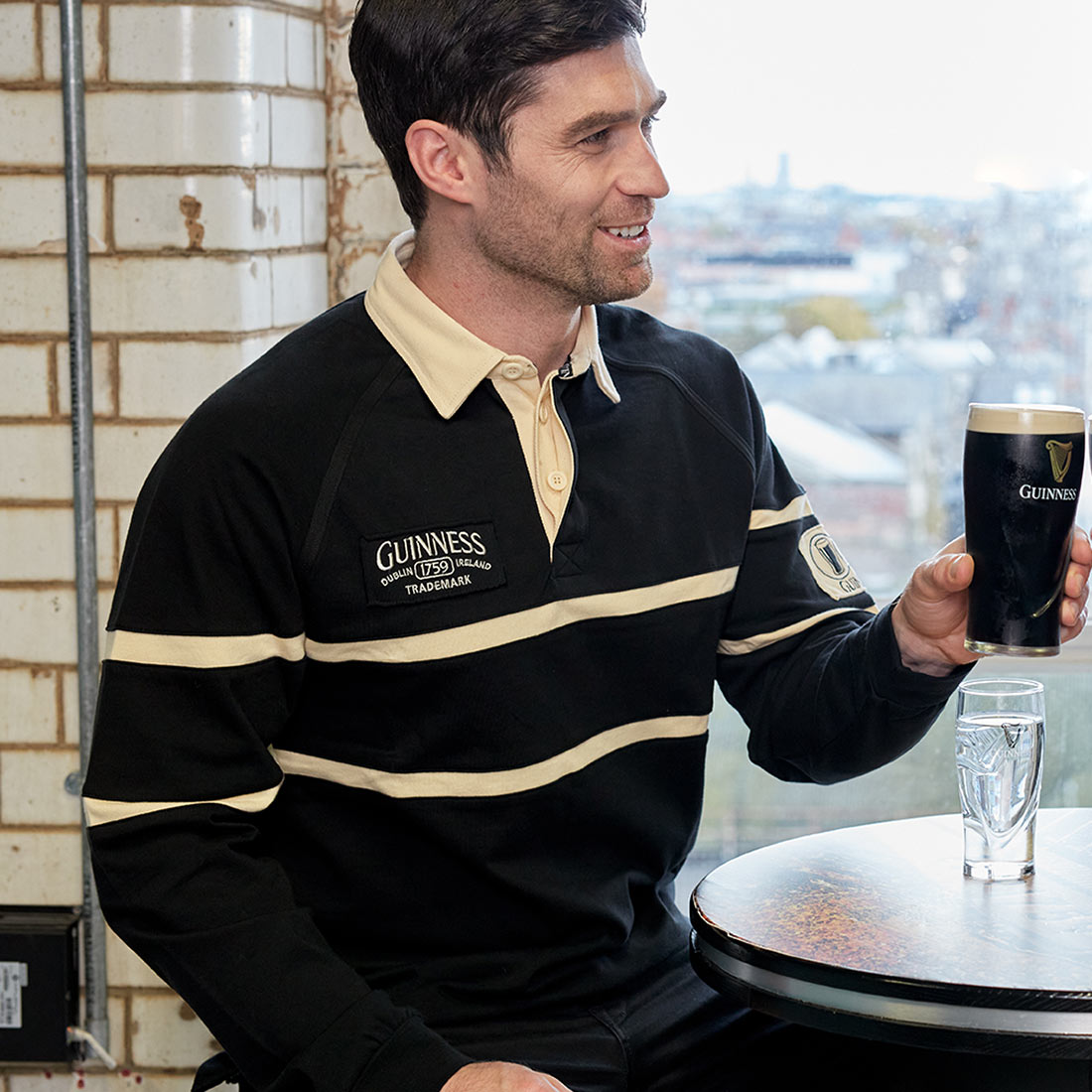 A man wearing a Guinness rugby jersey holding a pint of Guinness at a table.